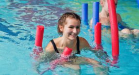 Groepje sporters in het zwembad die drijven met behulp van Pool Noodles