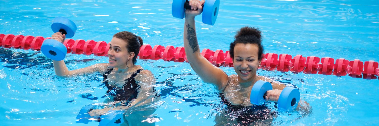 twee lachende vrouwen die aquarobics doen in hget zwembad met dumbells van foam