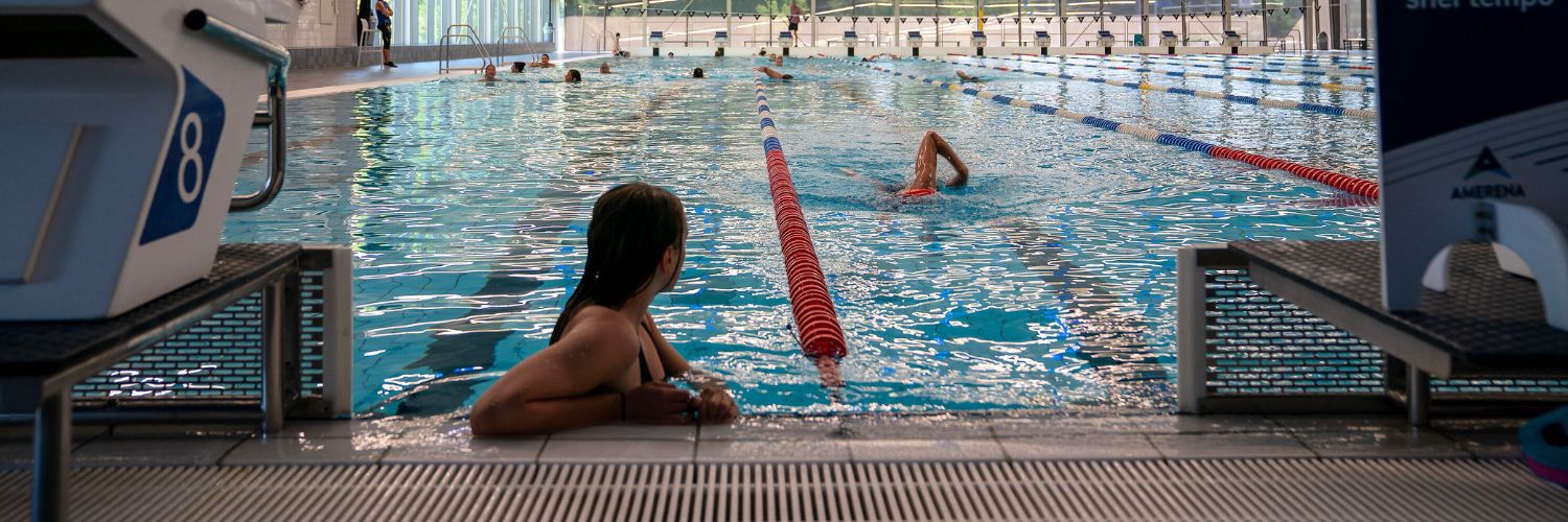 Overzicht van het 50 meter bad van Amerena tijdens het banenzwemmen. 1 vrouw leunt op de badrand