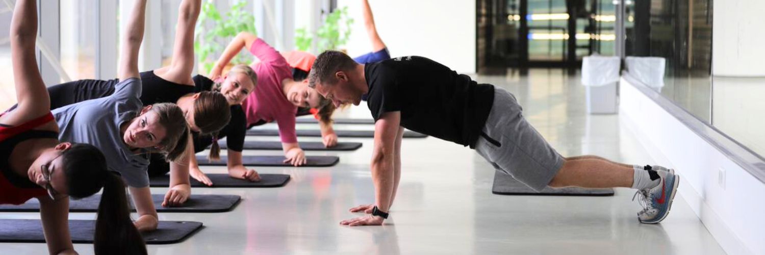 Groep doet een fitnessoefening liggend op een mat waarbij ze op 1 arm leunen en een arm in de lucht steken