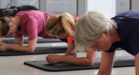 groep vrouwen doet oefening liggend op de vloer, leukend op de ellebogen.