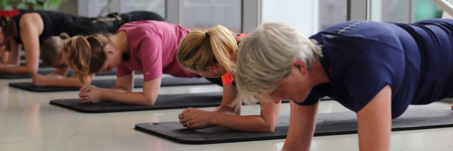 groep vrouwen doet oefening liggend op de vloer, leukend op de ellebogen.