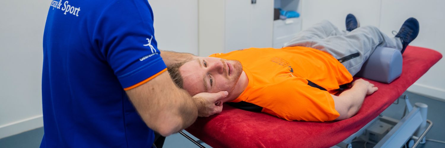 patient ligt op behandeltafel van de fysiotherapeut die zijn hoofd vast heeft tussen zijn handen