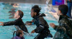 Kinderen springen van de kant af met kleren aan het zwembad in om te oefenen voor hun C diploma