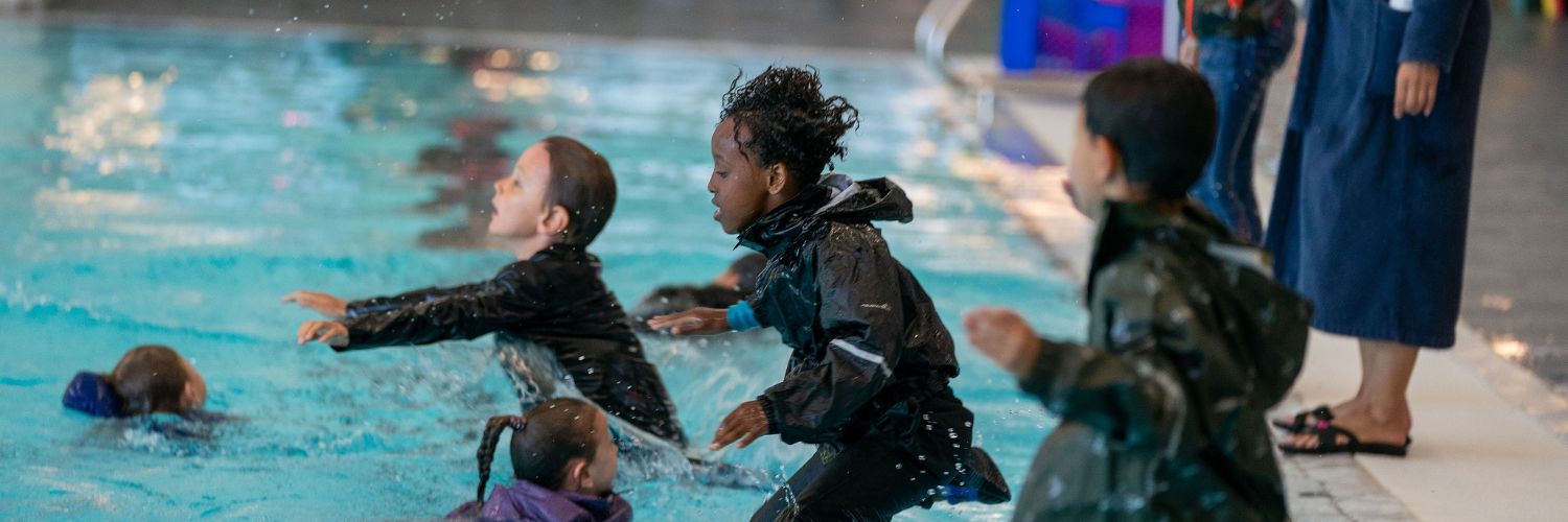 Kinderen springen van de kant af met kleren aan het zwembad in om te oefenen voor hun C diploma