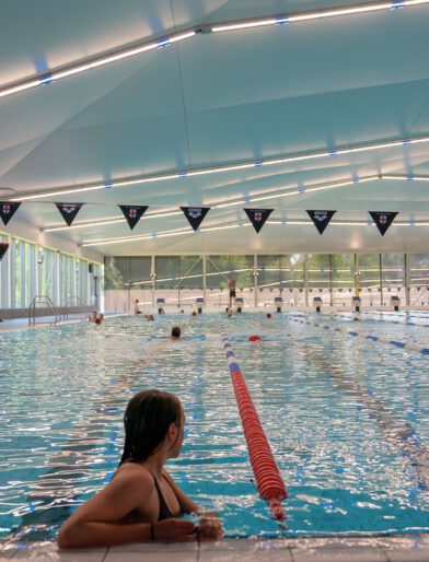 Vrouw leunt op badrand van het 50 meter bad in Amerena terwijl ze naar de andere zwemmers kijkt