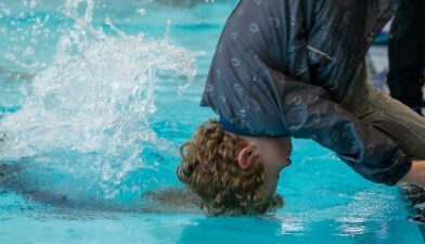 jongetje maakt koprol voorover in het zwembad gekleed in regenkleding