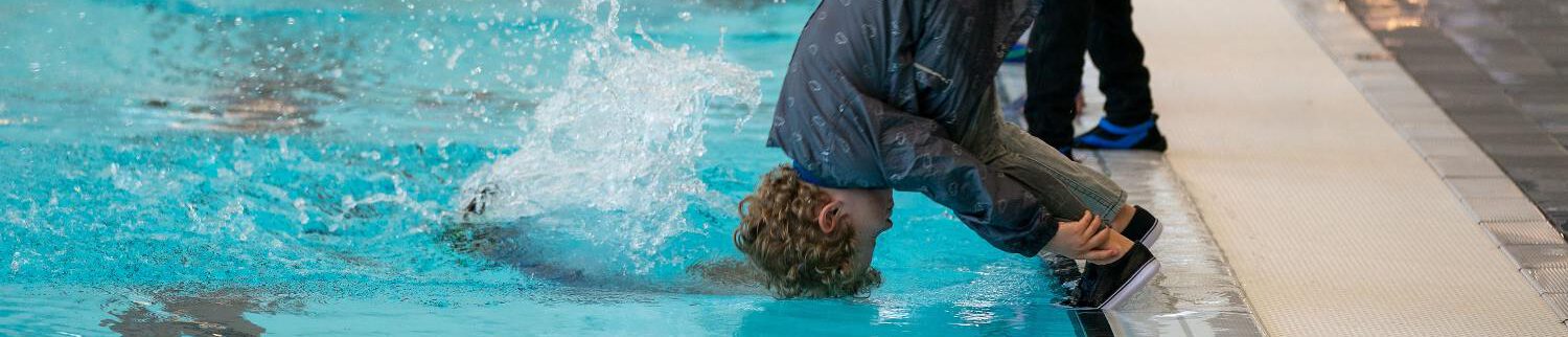 jongetje maakt koprol voorover in het zwembad gekleed in regenkleding